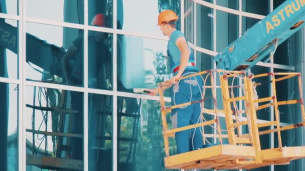 Рабочий стеклоочиститель на гидравлическом лифте моет окна — стоковое видео