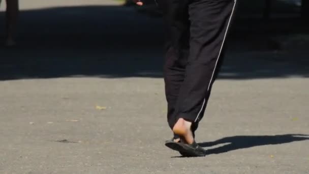 Мужчина идет по улице в черных трениках и шлепанцах — стоковое видео