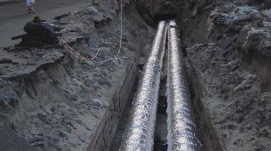 Isıtma tesislerinin borularıyla açık bir siper. Gümüş termal yalıtım