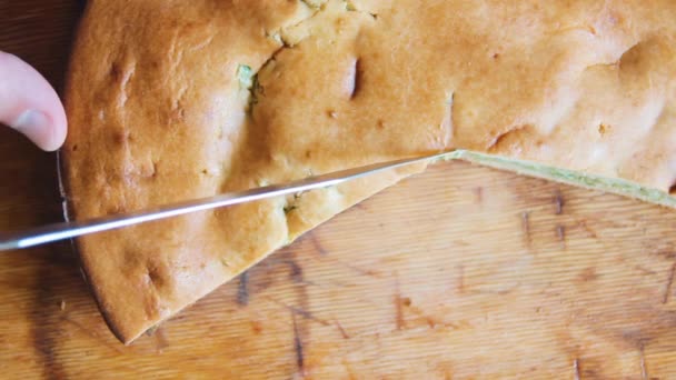 Eine halbe runde Zwiebelkuchen liegt auf einem Holztisch. Ein Mann schneidet mit der Hand eine Bäckerei — Stockvideo