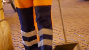 Elinde süpürge ve faraş olan bir yol işçisi kaldırımdaki döküntüleri temizliyor. Hizmetli