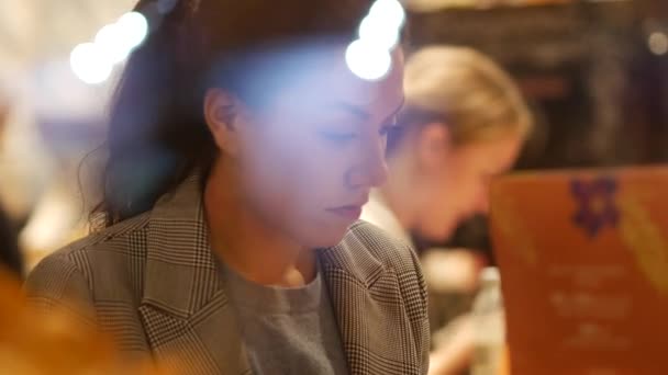 Uma menina senta-se em uma mesa de um café de rua pela janela no final da noite — Vídeo de Stock