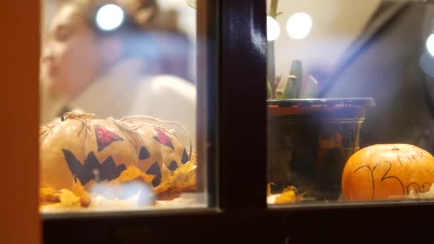 Citrouilles orange avec des symboles d'Halloween dans une fenêtre de café de rue. Derrière le verre — Video