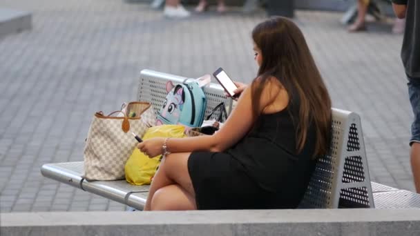 Curvyy jonge vrouw in het kort zwart jurk zit op de bank en praat aan de telefoon — Stockvideo