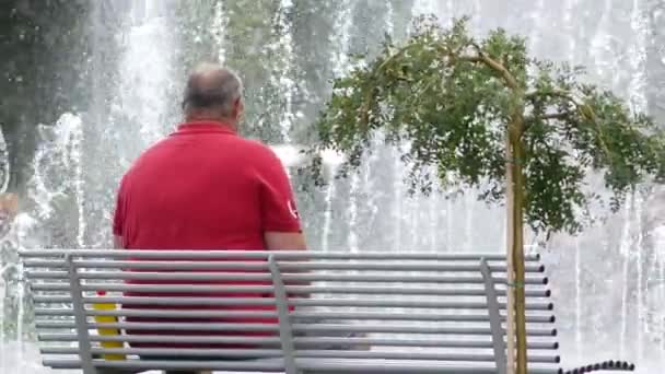 Mężczyzna w średnim wieku o wysportowanej budowie w czerwonej koszulce spoczywa na ławce. — Wideo stockowe