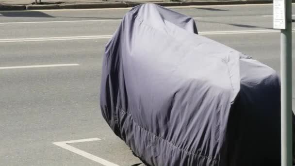 오토바이는 도로에 주차되어 보호용 방수포로 덮여 있습니다. 덮개 — 비디오