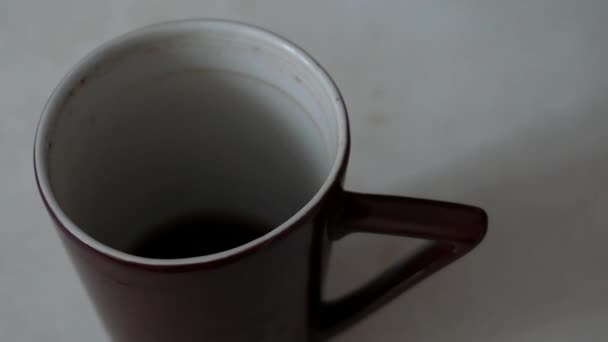 Mano del hombre tomando una taza de porcelana marrón con café sin terminar en la mesa. — Vídeos de Stock