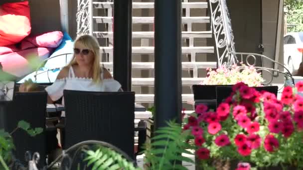 Young blond woman come to summer cafe. Waiter comes up and puts menu on table — Stock Video