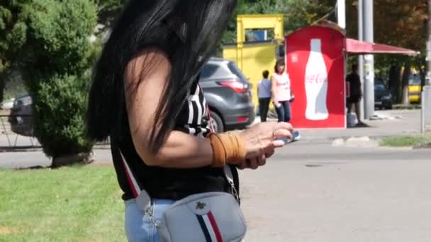 Молода жінка в шортах з довгим чорним волоссям пише повідомлення на смартфоні. — стокове відео