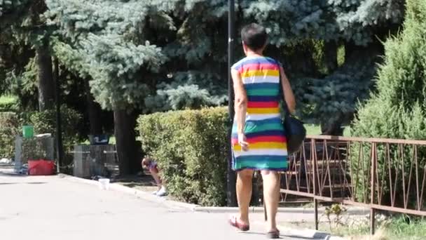 Egy színes csíkos ruhás nő sétál végig az utcán. Egy idős nő. — Stock videók