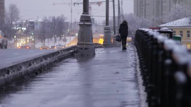 Şiddetli kar yağışı sonrası akşam şehri. Yapayalnız kadın, gün batımında Moskva Nehri 'nin köprüsünden geçiyor. Tarihi merkezin kışın güzel manzara manzarası. Soğuk Ocak kış günü. Araba trafiği