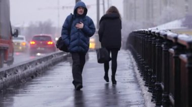 Yoğun bir kar yağışı sonrası akşam şehri. İnsanlar köprüden geçiyor.