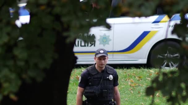 Hlídkový policista vedle auta. Muž v černé uniformě v neprůstřelné vestě a zbrani — Stock video