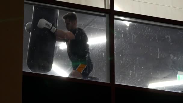 Muž trénuje v tělocvičně se závěsným boxovacím pytlem. Chlápek stávkuje a kopá. obrana — Stock video