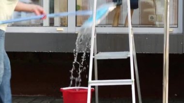 Kovası su dolu temizlikçi kadın camları temizliyor. Uzun saplı paspas