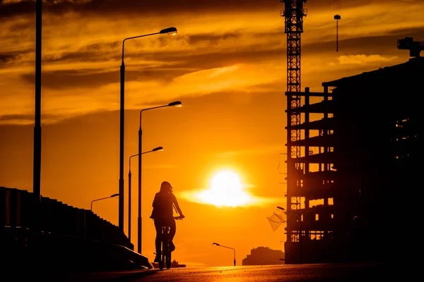 Silhouette eines Mädchens auf einem Fahrrad auf einer Brücke bei Sonnenuntergang — Stockfoto