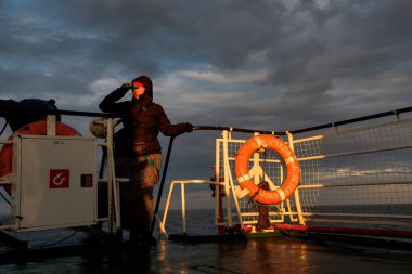 Bir kız bir gemide dürbün ile günbatımında görünüyor..