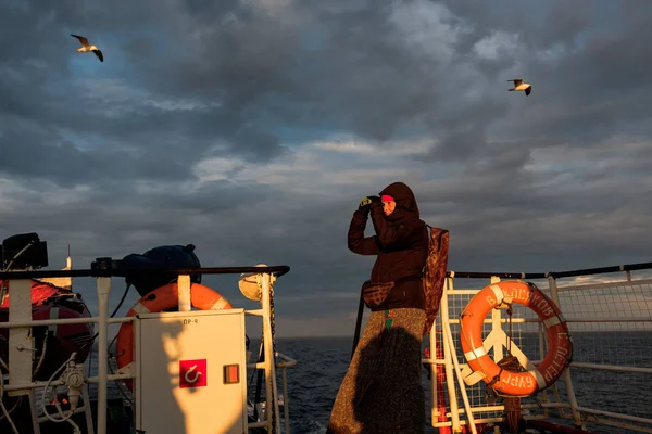 Bir kız bir gemide dürbün ile günbatımında görünüyor..