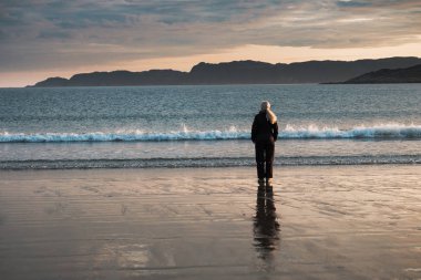 Gün doğumunda Barents Denizi kıyısında bir kız duruyor.