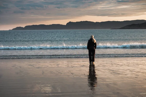 Gün doğumunda Barents Denizi kıyısında bir kız duruyor.