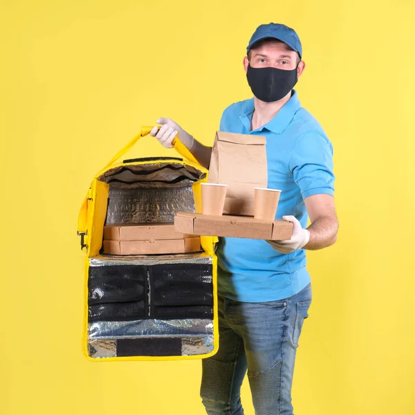 Courier con máscara de protección contra virus y guantes de entrega de alimentos médicos con bolsa de termo abierta amarilla sostiene una orden del restaurante para el cliente en el fondo del estudio amarillo. entrega segura de alimentos — Foto de Stock