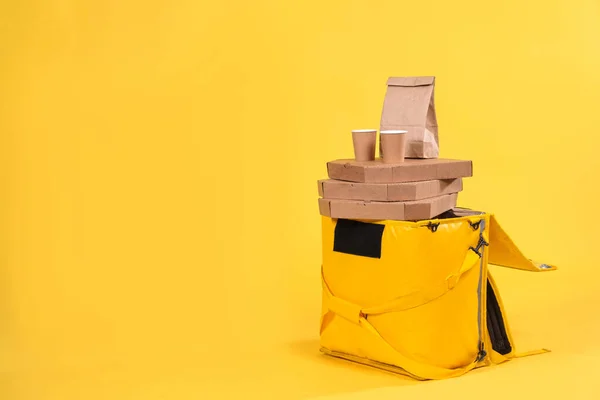 Yellow refrigerator bag for food delivery or for trip to nature and tourism on yellow background with food pizza and drinks in an eco-friendly paper packaging. Thermos bag protects food from spoilage.