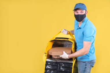 Virüs koruma maskesi takan kurye ve sarı termos çantalı tıbbi gıda dağıtım eldivenleri sarı stüdyo arka planında müşteri için restorandan sipariş veriyor. Güvenli yiyecek teslimatı.