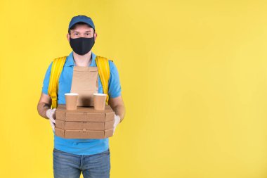 Koruyucu maskeli ve eldivenli genç yemek dağıtım elemanı restoran müşterisi için sipariş veriyor. Mavi polo gömlek giymiş ve omuzlarında sarı alışveriş çantası taşıyor. Güvenli teslimat..