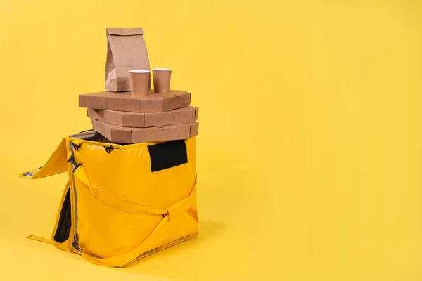 Yellow refrigerator bag for food delivery or for trip to nature and tourism on yellow background with food pizza and drinks in an eco-friendly paper packaging. Thermos bag protects food from spoilage.