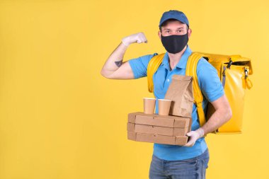 Yüzünde koruyucu siyah maske, mavi tişörtlü tıbbi eldivenler ve omuzlarında sarı termo çanta olan kurye restorandan emir alıyor ve kaslarını kasarak gücünü gösteriyor.