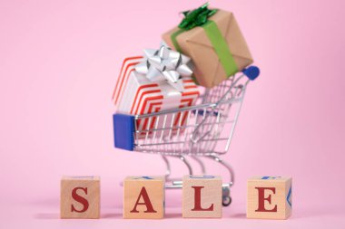 Kırmızı sözcüğün satışı, pembe arka planda yer alan, süpermarket market alışveriş arabalarıyla dolu ahşap küpleri hazırladı. Kara Cuma günü süpermarkette veya çevrimiçi mağazada ürün satma kavramı
