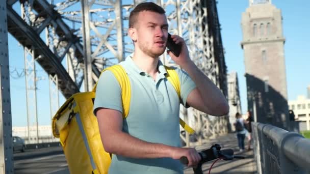 Correio de entrega de alimentos de restaurantes e alimentos de supermercados olha para o telefone e procura por sinal GPS para encontrar endereço de entrega e fala por telefone na ponte de ferro na cidade durante o dia — Vídeo de Stock