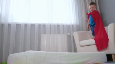 Kırmızı Süper Adam çocuk süper kahraman pelerin çocuk odasında yatarken sandalyeden yatağa atlıyor. Süper kahramanın düşüşü, çocukların uçma girişiminde başarısız olması, çocukların hayal gücü. Yavaş çekim videosu