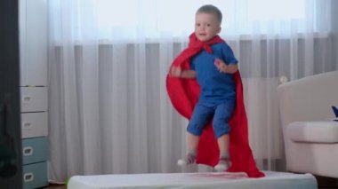 Sarışın, beyaz çocuk süper kahraman kahraman çocuk eğleniyor ve trambolinde olduğu gibi yatakta zıplıyor, çocukluğunda eğleniyor ve eğleniyor, seyahat konseptiyle seyahat ediyor.