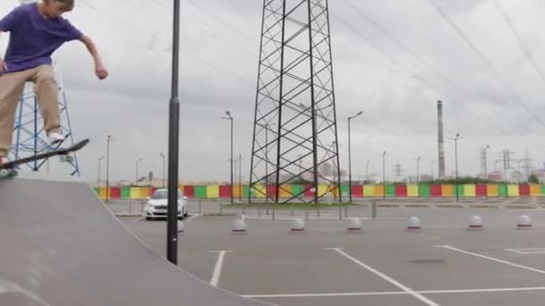 Junger Teenager mit langen blonden Haaren fährt Skateboard im Skatepark. Skateboarder rutscht hohe Rampenrutsche in gerader Linie hinunter und macht verschiedene Tricks, springt bei trübem Wetter auf dem Skateboard auf — Stockvideo