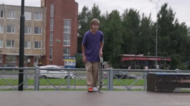 Profi-Skater-Teenager treibt Extremsport im Skatepark und macht Tricks, Skateboarder junger blonder Junge fährt Skateboard und springt im Sommer bei trübem Wetter von großer Höhe zu Boden. — Stockvideo