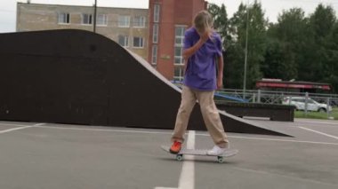 Profesyonel kaykaycı genç, bir kaykay parkında ekstrem sporlar yapıyor. Sarışın genç kaykaycı çocuk bulutlu bir havada kaykay parkında öne doğru kayıyor. Yavaş çekim videosu