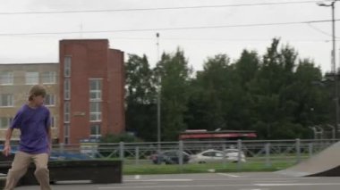 Profesyonel kaykaycı genç, kaykay parkında ekstrem sporlar yapıyor. Genç sarışın kaykaycı çocuk bulutlu bir havada kaykay parkında öne doğru kayıyor..