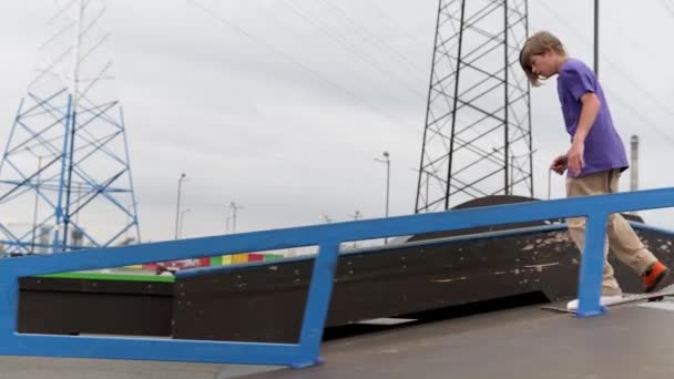 Junge blonde Skateboarder fahren bei trübem Wetter auf Skateboard im Skatepark vor. Profi-Skater-Teenager treibt Extremsport im Skatepark und führt Tricks vor. — Stockvideo