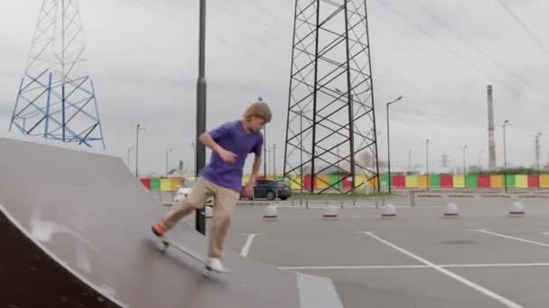 Профессиональный подросток катается на скейтборде в скейт-парке. Скейтбордист скользит по высокой рампе по прямой и делает различные трюки, прыгая на скейтборде в облачную погоду — стоковое видео
