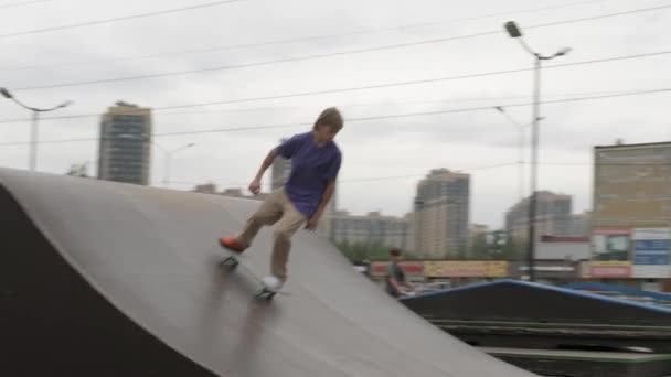 Patinador profesional adolescente se dedica a paseos rubios monopatín en el parque de skate. Skateboarder se desliza por la rampa alta en línea recta y hace varios trucos, rebotando en el monopatín en tiempo nublado — Vídeos de Stock