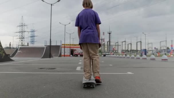 Mozifilm. Fiatal szőke fiú profi gördeszkás lovagol gördeszka az úton a gördeszka park. A tinédzser veszélyes és traumatikus extrém ifjúsági sportban vesz részt.. — Stock videók