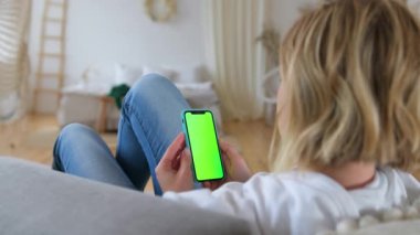 Kromakey yeşili akıllı telefon ekranı tutan sarışının arka görüntüsü. Cep telefonu kullanan, internette sosyal ağlara göz atan, yatakta yatan bir kadın. St. Petersburg, Rusya, Aug, 2020