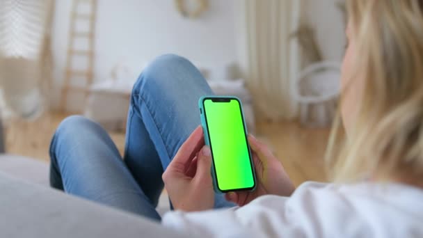 Frau benutzt Handy, surft in sozialen Netzwerken im Internet, liegt im Bett. Rückansicht der Blondine mit dem chromakey-grünen Smartphone-Bildschirm. St.Petersburg, Russland, Aug, 2020. — Stockvideo