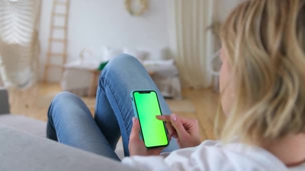 Girl using phone, internet social networks browsing. Woman at home lying on couch using smartphone with green mock-up screen, scrolling gestures, doing swiping. St.Petersburg, Russia, Aug, 2020 — Stock Video