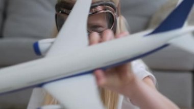 Evinde beyaz oyuncak yolcu uçağıyla oynayan bir pilotun gözlükleriyle gülümseyen güzel sarışın kızın yakın plan portresi. Dünya turizm, dinlenme ve seyahat kavramı.