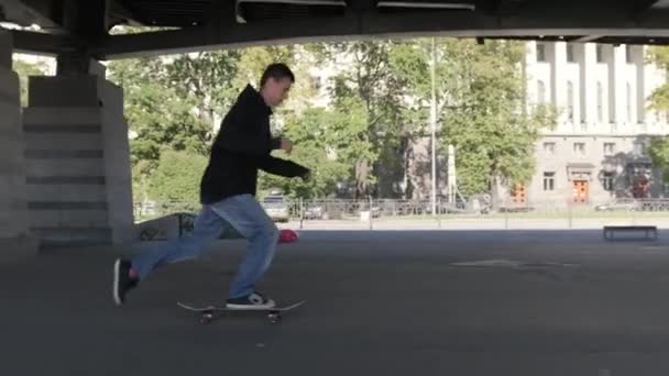 Teenager βόλτες στο πίσω τροχούς του skateboard εκτελεί κόλπα ισορροπίας στο χώρο του skate Park κάτω από μια σιδερένια γέφυρα. Επαγγελματίας skateboarder τύπος με σκούρα ρούχα εκτελεί ένα τέχνασμα για skateboard — Αρχείο Βίντεο