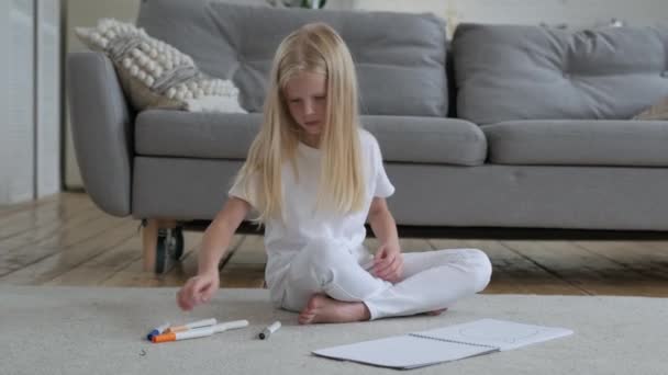 A gyerek úgy csinálja a házi feladatot, hogy otthon papírra rajzolja a markereket. Csinos kaukázusi szőke művész lány egyedül rajzol színes markerek fehér album lap papír, egyenesíti a hosszú szőke haj. — Stock videók
