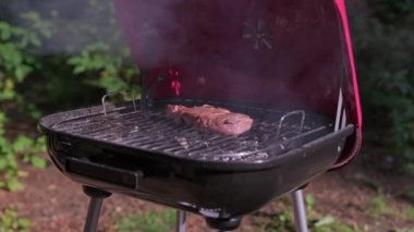Yavaş çekim şefi ızgarayı açıyor, tong kullanıyor ve eti ızgarada pişiriyor. Ateş yanıyor, biftekli sığır filetosu pirzola barbeküde pişiyor. Orta boy ızgara, lezzetli biftek yakın çekim..