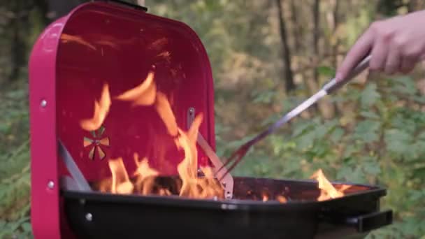 Slow motion video przygotować grill do gotowania mięsa i warzyw na wakacjach. Duży płomień z ogniem płonącym w grillu. Gorący węgiel płonie w kozieradce, a kucharz miesza gorący węgiel żelaznym widelcem.. — Wideo stockowe
